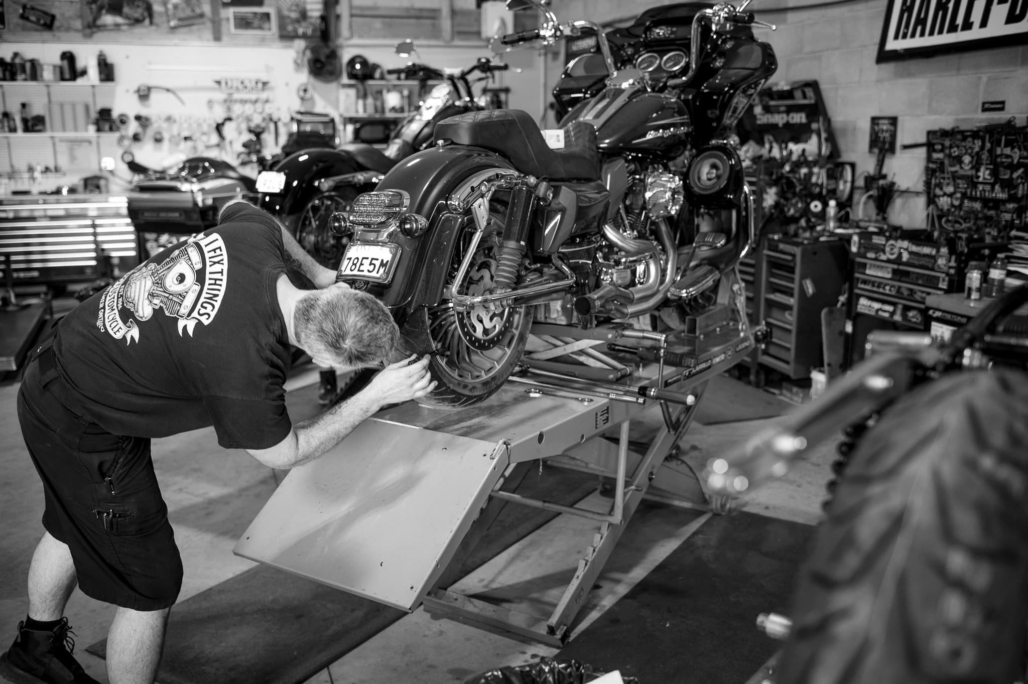 Tech leaning into a Touring rig on the service lift, black-and-white shop action