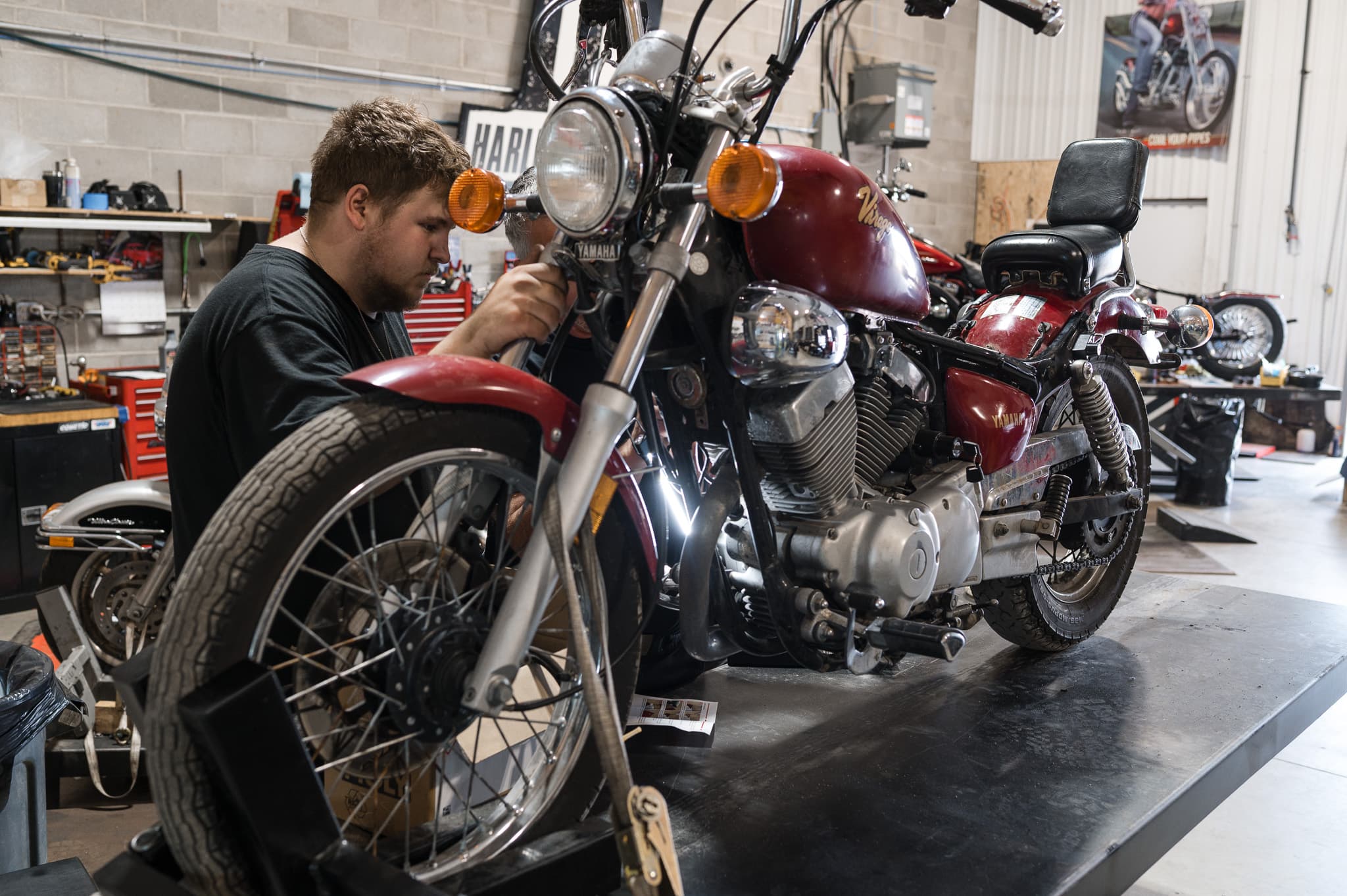 Tech wrenching on the front end of a red Harley-Davidson Sportster