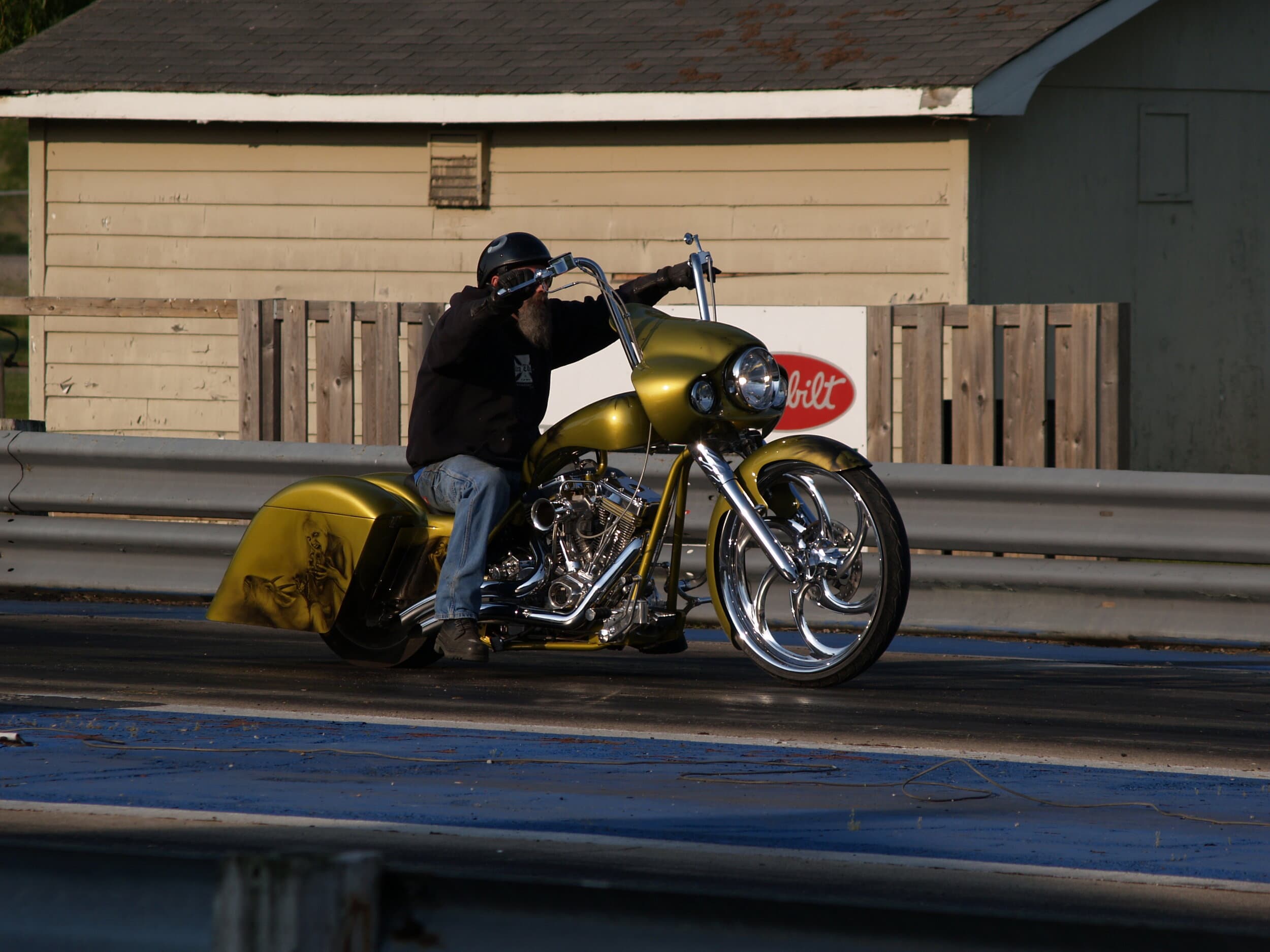 Rider launching a gold Harley bagger down the strip, performance and power on display