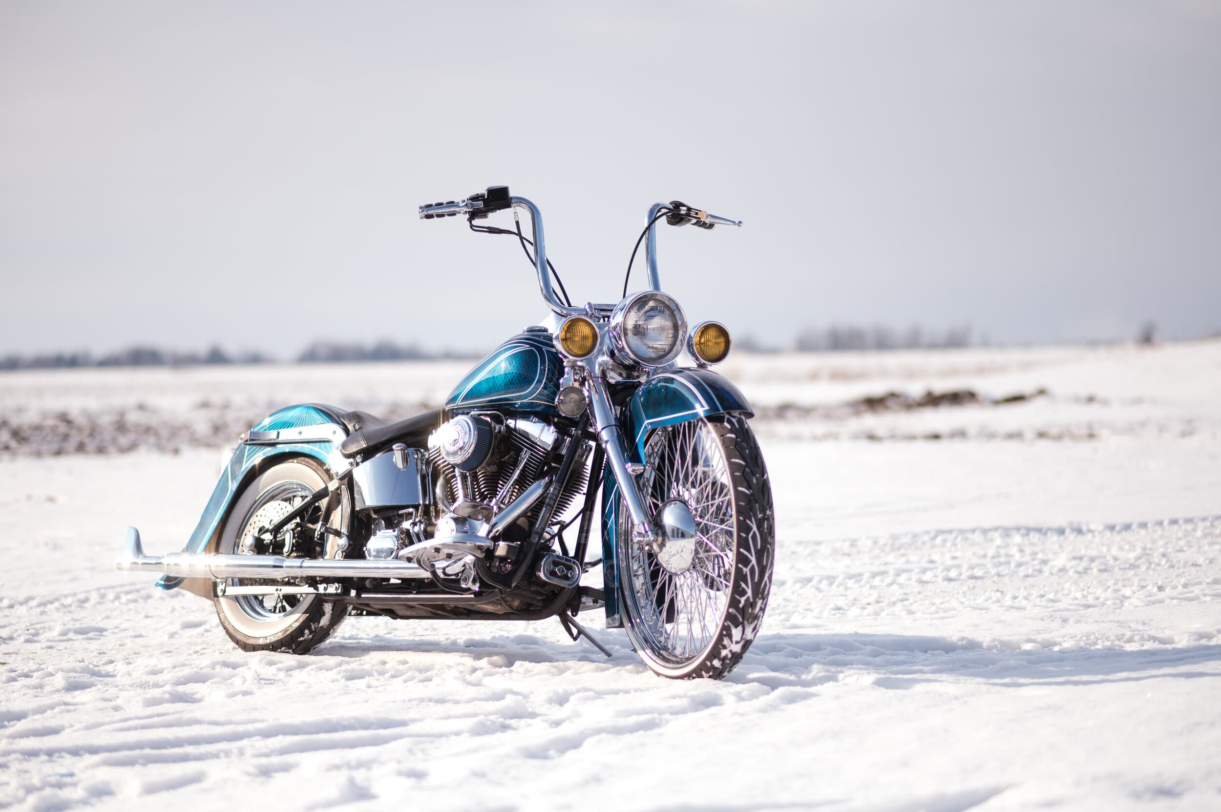 Front end of a custom Harley parked on snow, chrome and headlight detail