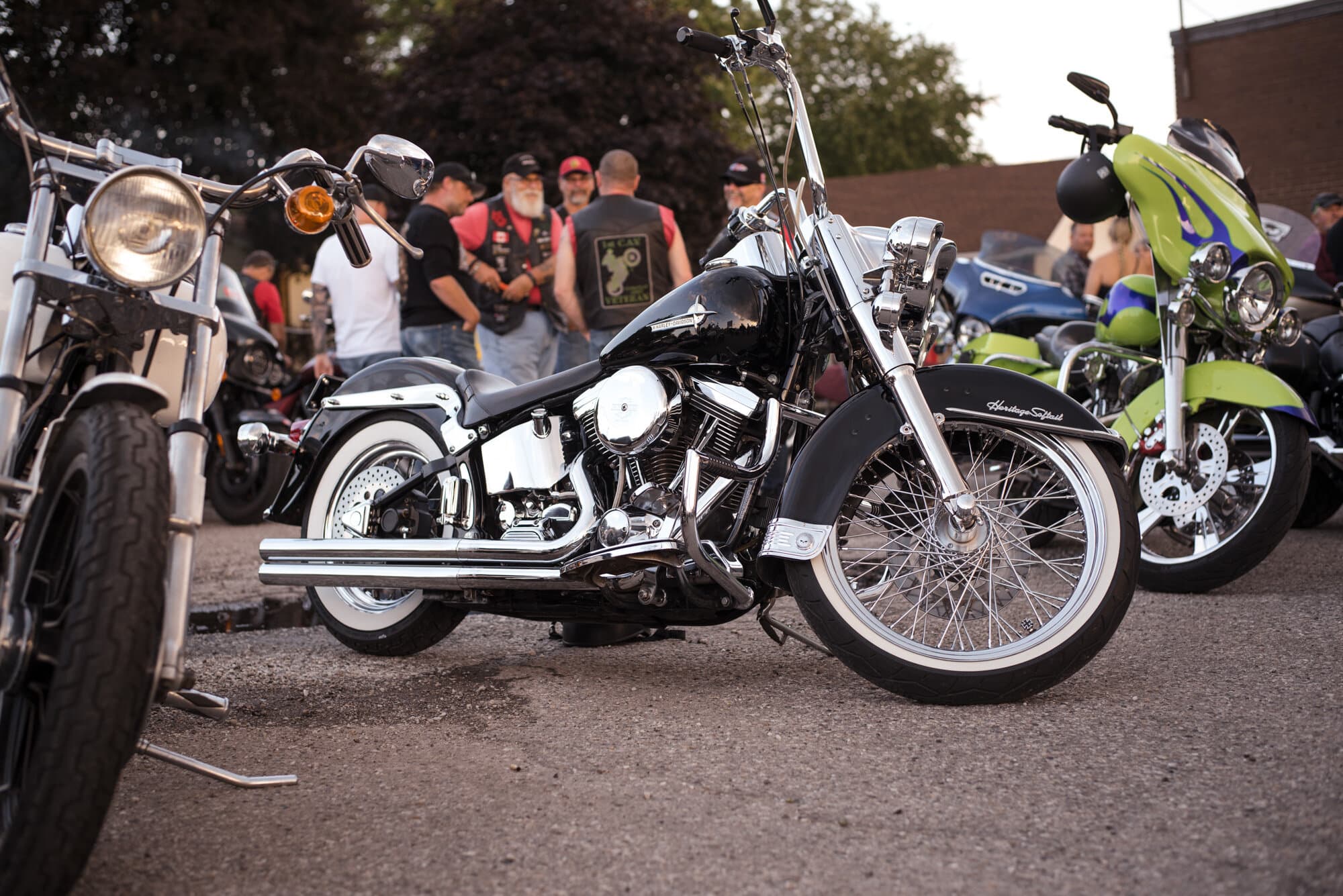 Black Harley Softail at an evening bike night with riders gathered in the background